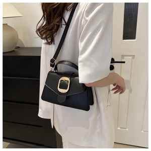 Close-up of black lychee leather bag with large golden metal buckle and shoulder strap