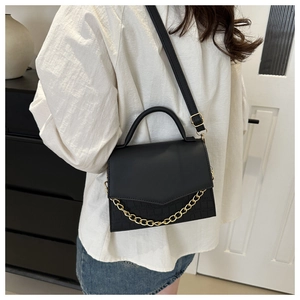 Detailed view of black crossbody bag with gold chain and crocodile texture on a model