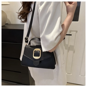 Detail of black pebbled leather bag with prominent gold square buckle and adjustable strap
