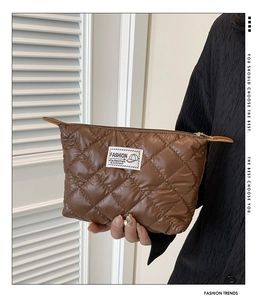 Dettaglio di una trousse marrone in nylon trapuntato con etichetta moda e cerniera superiore