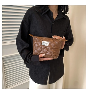 Détail d'une pochette matelassée marron avec broderie élégante tenue par un modèle