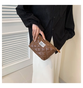 Dettaglio di una pochette in nylon marrone trapuntato con trama a rombi ed etichetta moda