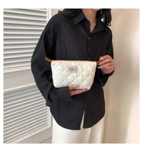 Dettaglio della borsa trapuntata color crema con etichetta FASHION e camicia nera chic