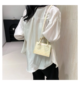 Detail of a quilted cream crossbody bag styled with a white shirt and black trousers