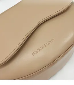 Detailed close-up of textured beige leather saddle bag featuring an embossed brand logo