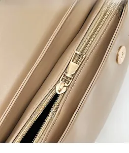 Close-up of golden smooth metal zipper and polished hardware on beige leather bag