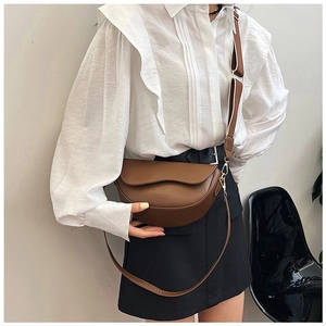 Detail of dark brown leather saddle bag with wide shoulder strap and gold hardware