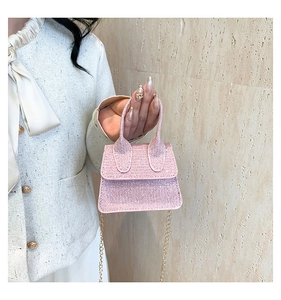 Detail of pink glitter mini handbag with elegant gold chain and top handle on a textured wall