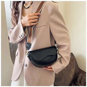 Detail of black leather saddle bag with wavy flap design and wide striped fabric strap