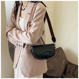 Detail of black saddle bag with brown strap styled on a model in a beige suit