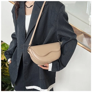 Detailed shot of beige leather saddle bag featuring a gold-toned metal strap attachment