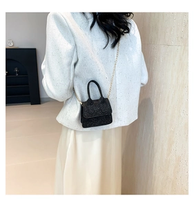 Close-up of black glitter mini handbag with elegant gold chain strap worn by a model