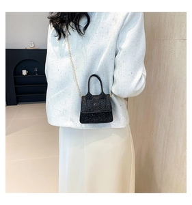 Detail shot of a black sequin mini handbag with a delicate gold chain on a white tweed jacket