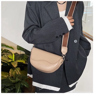 Detail view of beige saddle bag featuring an embossed logo and wide patterned strap