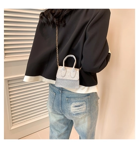 Rear view of model holding a glittery silver mini handbag with gold chain strap