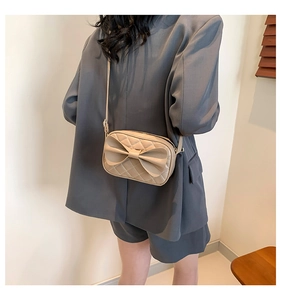 Vue latérale du sac à bandoulière matelassé beige avec un grand nœud sur un mannequin