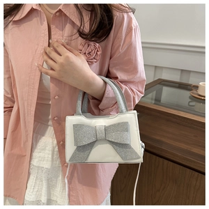 Detailansicht einer weißen Lederhandtasche mit einer großen, glitzernden silbernen Schleife