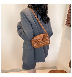 Détail d'un sac bandoulière marron avec nœud décoratif et coutures blanches en losange