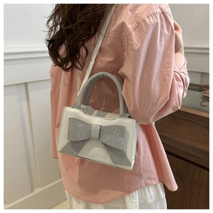 Detailansicht einer weißen Handtasche mit großer silberner Paillettenschleife am Model