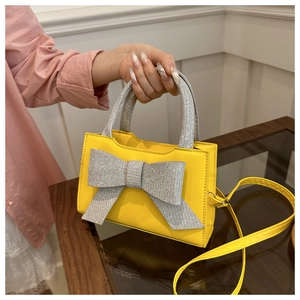 Detail einer hellgelben Handtasche mit einer großen, funkelnden silbernen Pailletten-Schleife