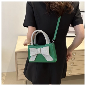 Rückansicht einer grünen Mini-Tasche mit großer silberner Glitzerschleife und Riemen