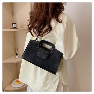 Close-up of black crocodile-embossed handbag with rigid top handle and textured finish
