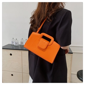 Side view of vibrant orange crocodile pattern bag worn by a model in a dark suit