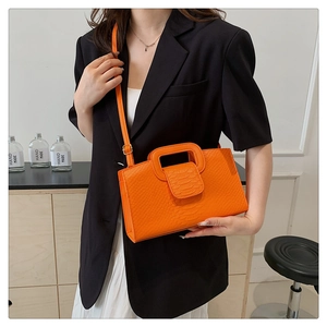 Detail of bright orange crocodile texture handbag with cutout handle and shoulder strap