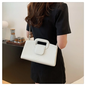 Detailed view of a white crocodile-embossed handbag with square handle and slim strap