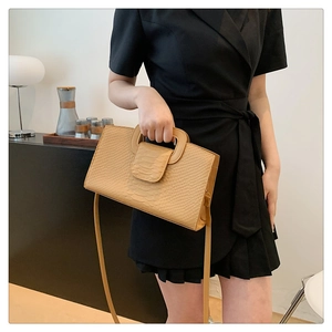 Detail of camel crocodile-textured handbag featuring unique trapezoid handle and shoulder strap