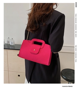 Model wearing a fuchsia crocodile embossed handbag with a gold chain strap and metal buckle