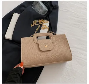 Detail of crocodile embossed faux leather handbag with gold chain and cutout handle