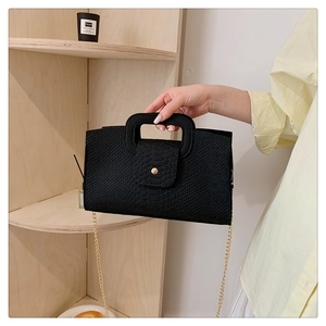 Detail of black crocodile texture handbag with gold chain strap and square handle