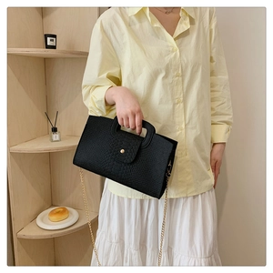 Detail of black crocodile pattern handbag with gold chain strap on a wooden shelf