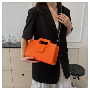 Detail of orange crocodile pattern handbag with gold chain strap worn by a model