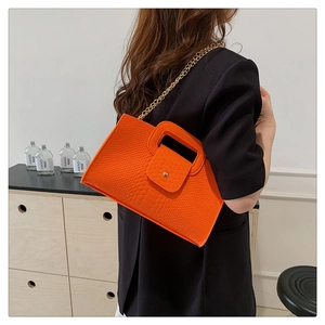 Detail of orange crocodile pattern trapezoid handbag with gold chain on model