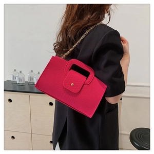 Detail of rose red crocodile pattern handbag with gold chain strap on black blazer
