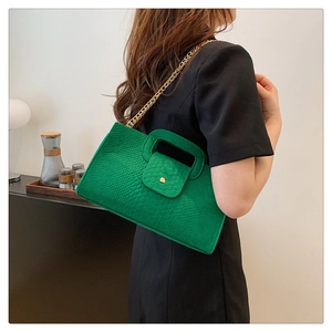 Detail of green crocodile pattern handbag with gold chain and cutout handle on black dress