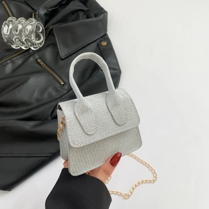 Mini silver glitter handbag with hard handle and gold chain strap held by hand