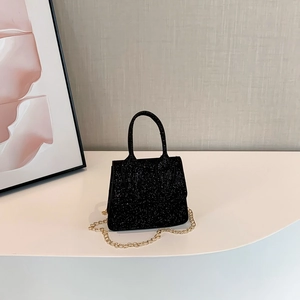 Chic black mini crossbody bag with glitter finish and elegant gold chain on white podium