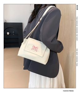 Close-up of a white shoulder bag with a pink butterfly embroidery and chain strap details