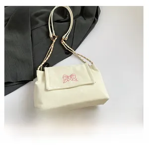 Detailed view of cream shoulder bag with pink butterfly embroidery and metal chain strap