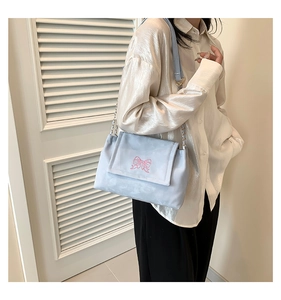 Detailed close-up of light blue shoulder bag featuring pink embroidered bow and chain strap