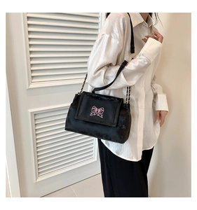 Close-up of black velvet shoulder bag with pink embroidered bow and chain strap details