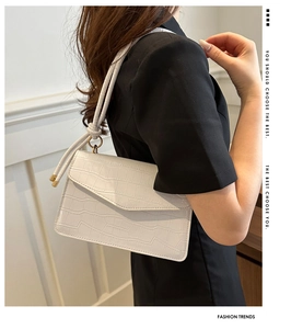 Detail of white crocodile pattern shoulder bag with golden metal hardware and strap