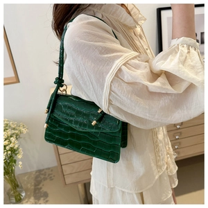Detail of dark green crocodile pattern leather crossbody bag with metallic accents