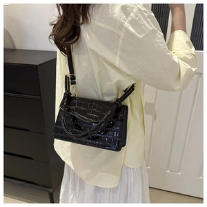 Detail of black crocodile texture handbag worn by a model in a cozy home setting