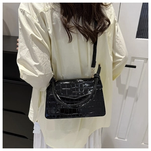 Detail of black crocodile texture leather crossbody bag with top handle and strap