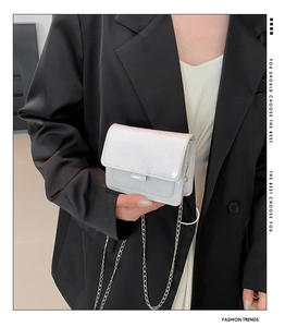 Détail du mini sac carré blanc pailleté avec bandoulière chaîne tenu par un modèle