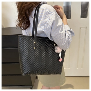Quilted black tote bag detail with fashion tag, gold rivets and pink plush pom-pom charm